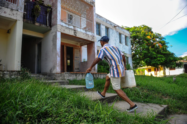 A man carries two large jugs of water to an apartment building.