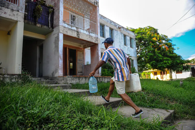 A man carries two large jugs of water to an apartment building.