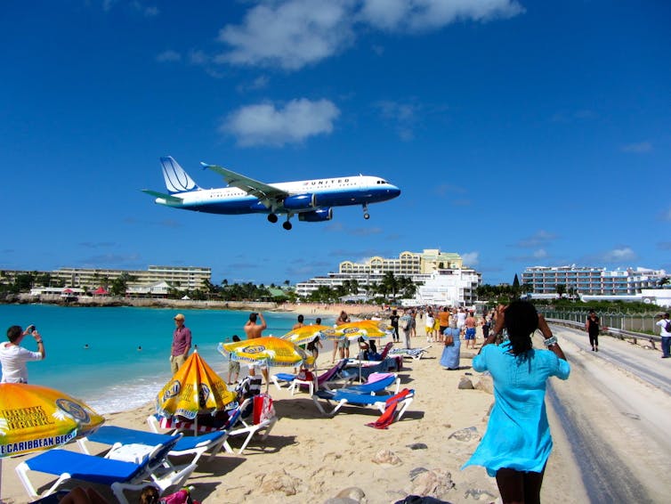 People on a beach with a large plane landing and hotels in the background in Sint Maarten.