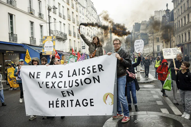 People at a protest carrying a white banner written in French