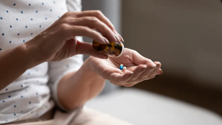 Closeup photo of a woman's hands with a prescription bottle and two blue and white capsules