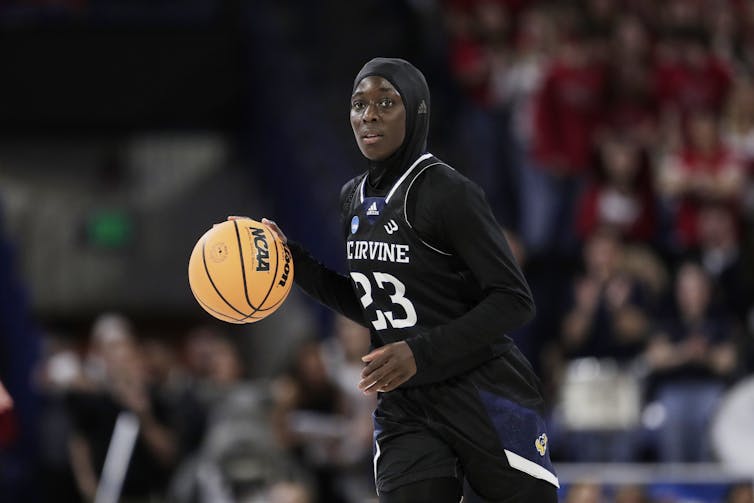 A young woman with her hair covered handling a basketball during a game.