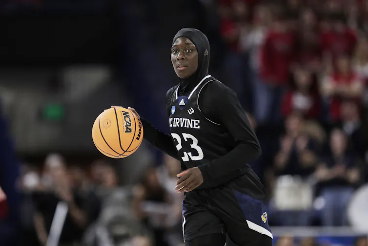 A young woman with her hair covered handling a basketball during a game.