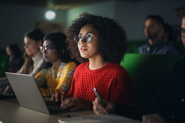 A young black woman in a lecture hall sitting with a laptop.