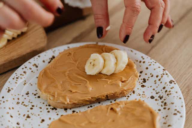 Person puts banana on toast with peanut butter