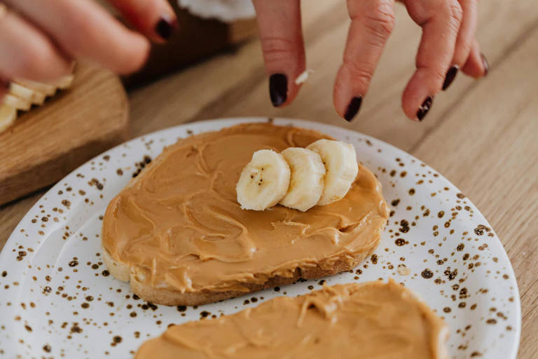 Person puts banana on toast with peanut butter