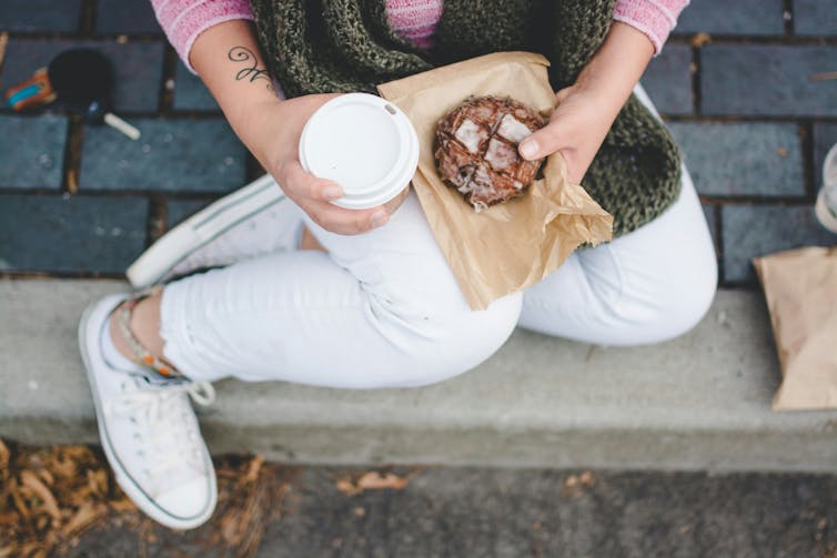 The woman holds coffee and pastries.