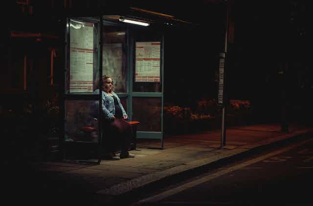 A woman sits alone at a bus stop at night