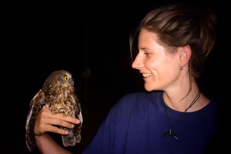 One of the authors, Victoria (Flossy) Sperring, holding a Norfolk Island morepork tagged for research, against a dark night sky