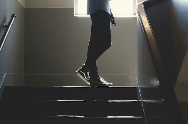 A man stands at the top of a dimly lit staircase. 