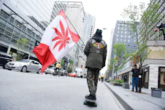 Man rides skateboard while carrying Canadian-style flag depicting a marijuana leaf