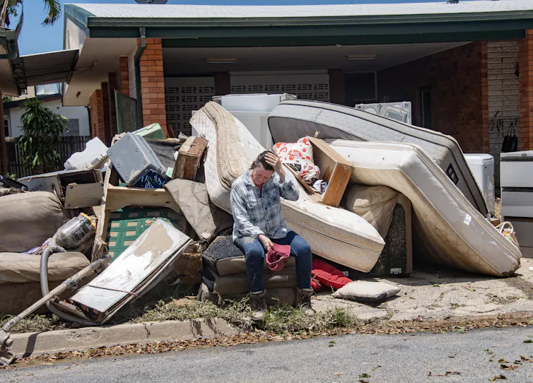 A woman sits on flood damaged furniture.
