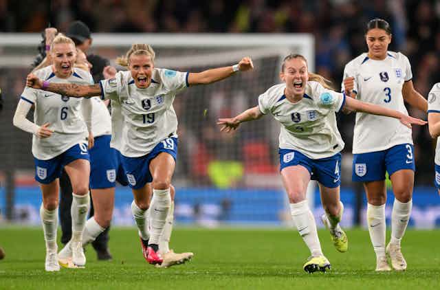 A group of England women footballers celebrate with arms spread. 