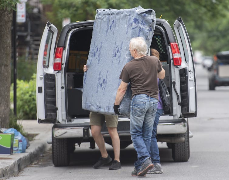 Two men remove a mattress from the back of a van.