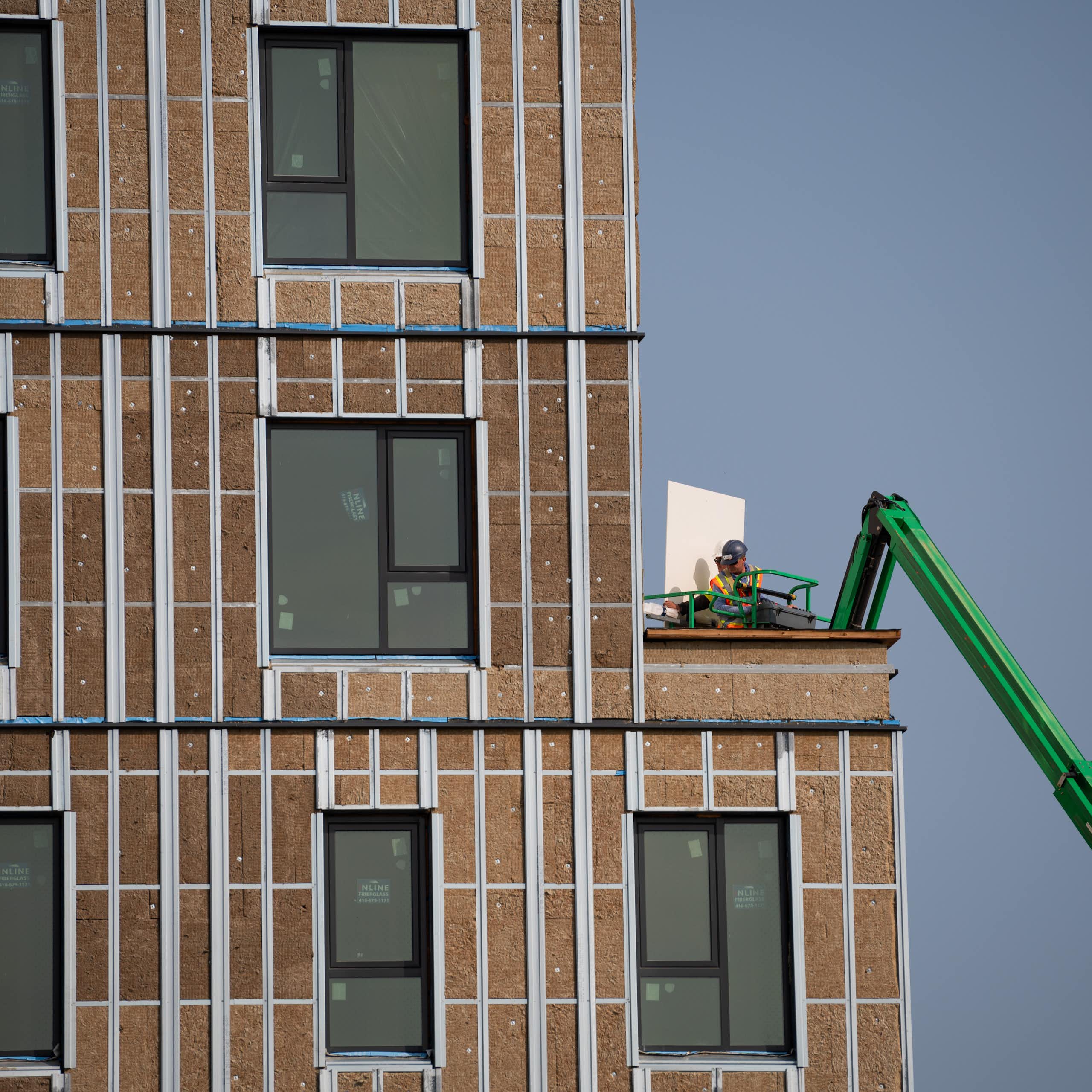 A construction worker uses a boom lift to move materials at a building under construction.