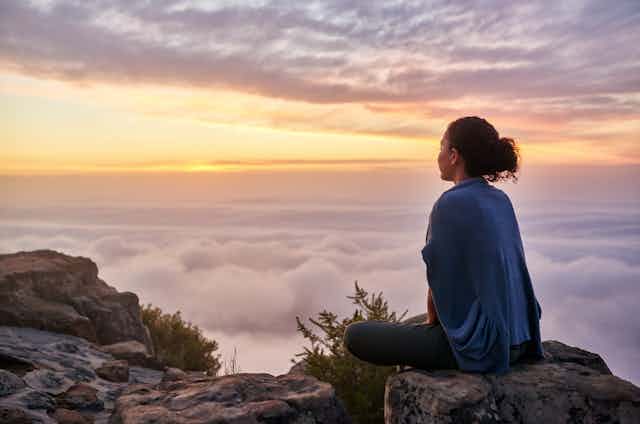 Photo d'une femme assise au sommet d'une montagne regardant un lever de soleil sur des nuages.