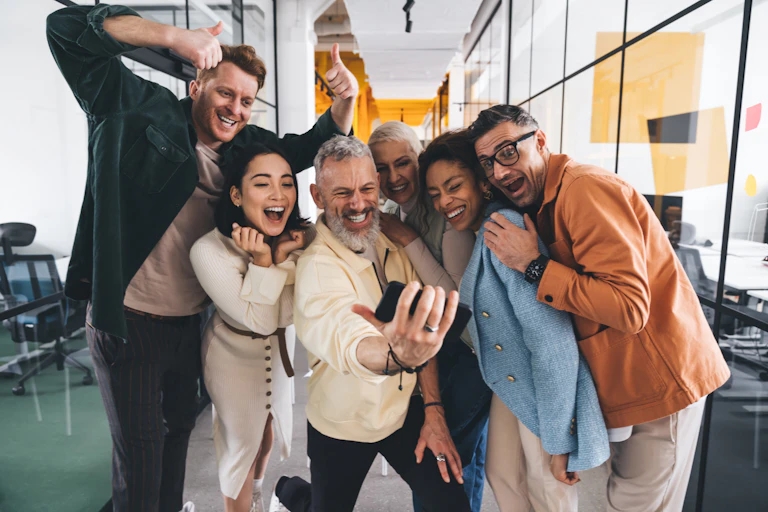 A group of smiling coworkers taking a selfie together in the office