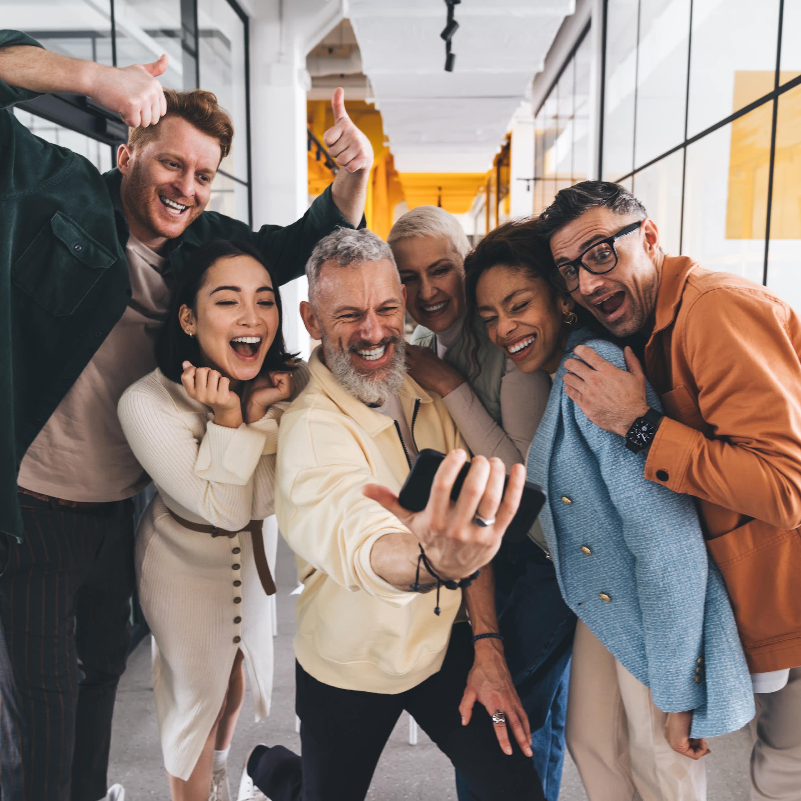A group of smiling coworkers taking a selfie together in the office