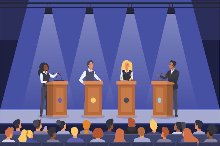 Four people on stage behind lecterns, in a meeting hall.