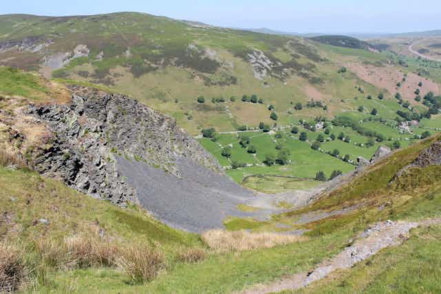 Wide green hilly landscape with black scree on hill in foreground