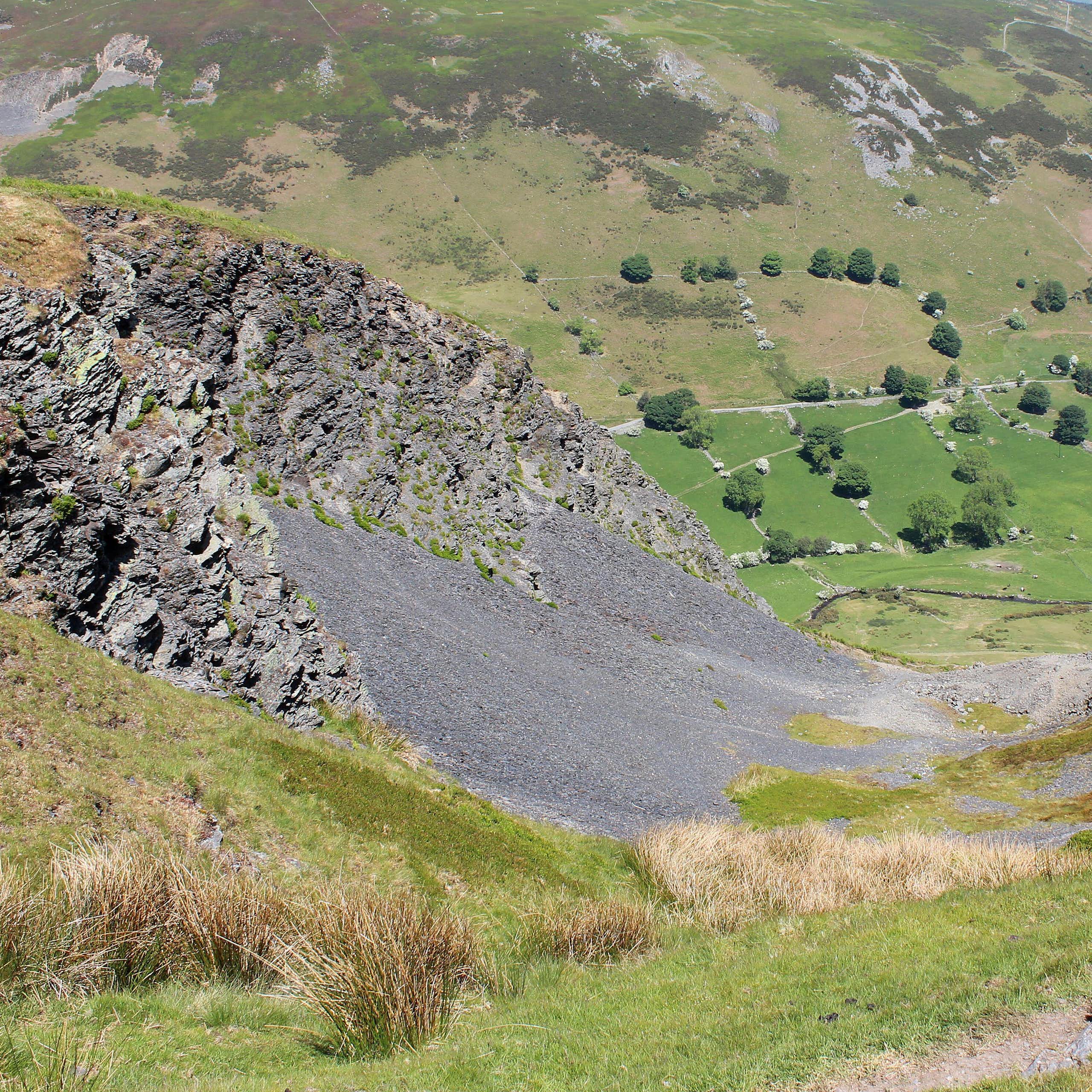 Wide green hilly landscape with black scree on hill in foreground