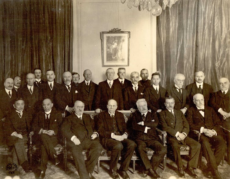 Two rows of men in suits posing in front of a painting