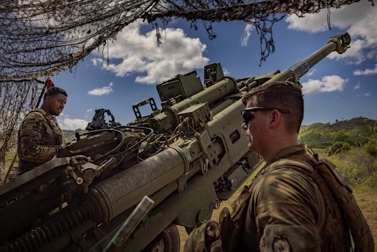 Men in fatigues stand by a missile launcher.