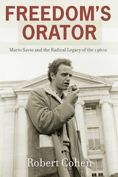 Mario Savio holding a microphone and a pencil as he speaks outside a building at University of California at Berkeley in the 1960s.