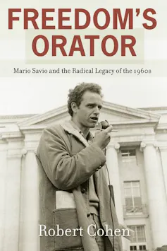 Mario Savio holding a microphone and a pencil as he speaks outside a building at University of California at Berkeley in the 1960s.