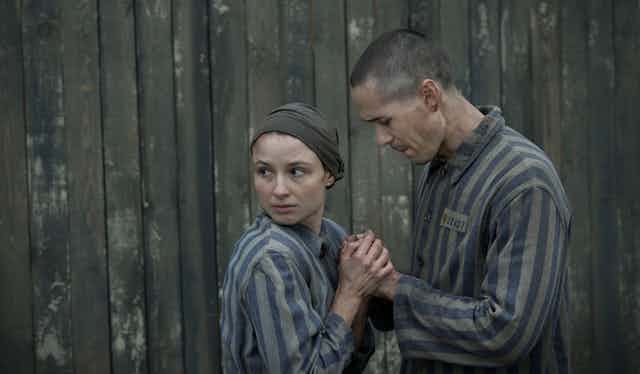 Man and woman in concentration camp uniforms hold hands