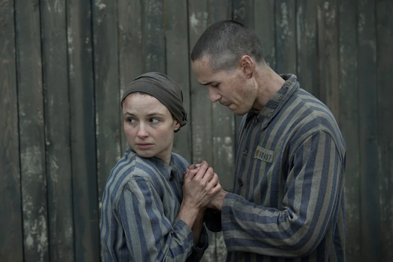 Man and woman in concentration camp uniforms hold hands