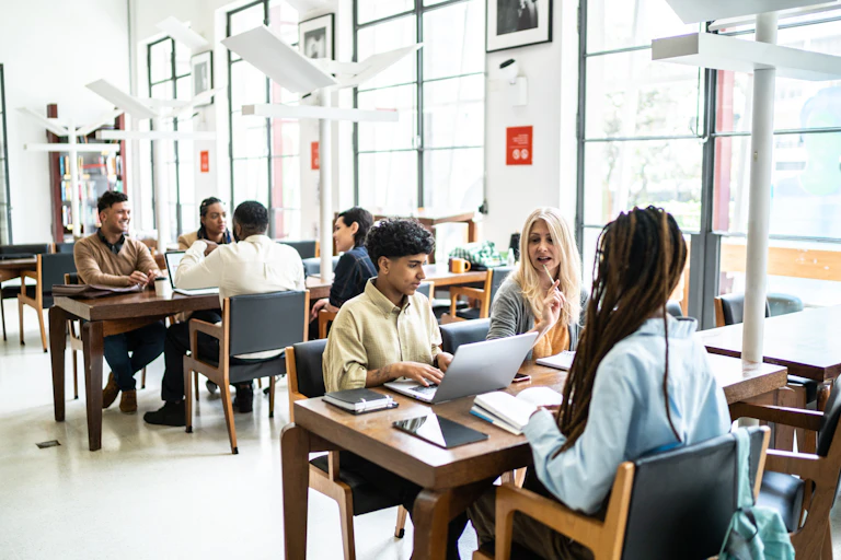 College students sit at tables with laptops and tablets.