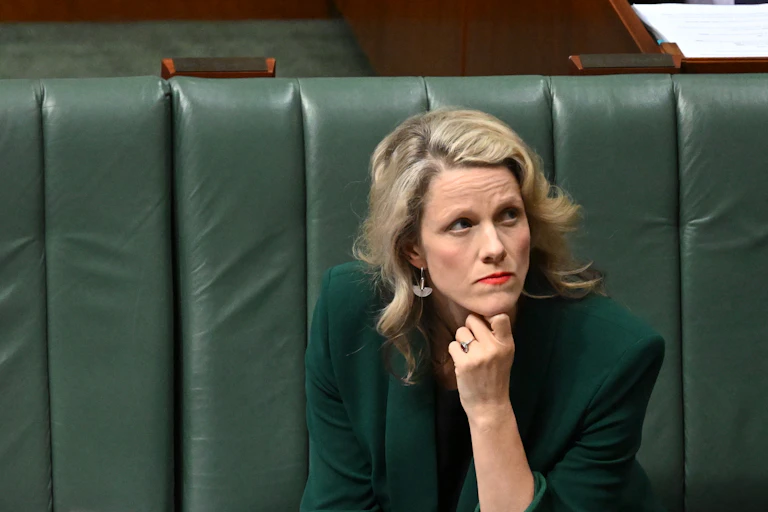 A blonde woman sits on a green couch with her hand on her chin