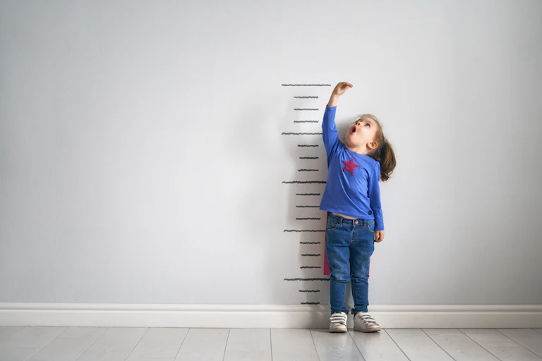 Little girl in cape measuring her height on wall chart.