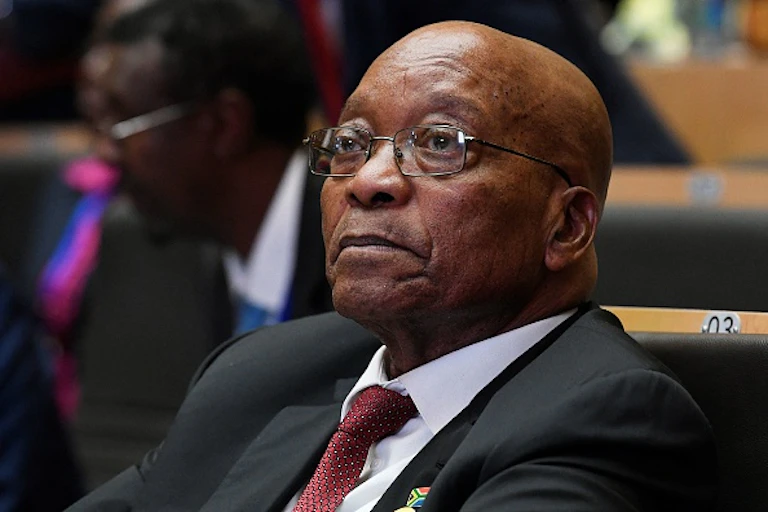 A man wearing a tie and specs looks ahead, listening to a speech.