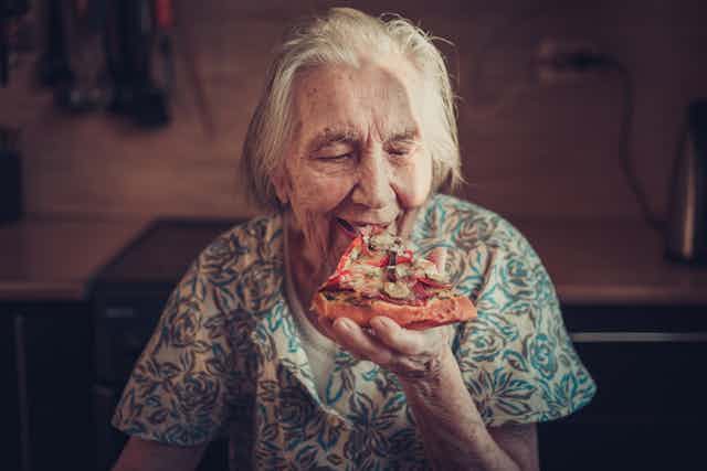 Elderly woman eating a slice of pizza