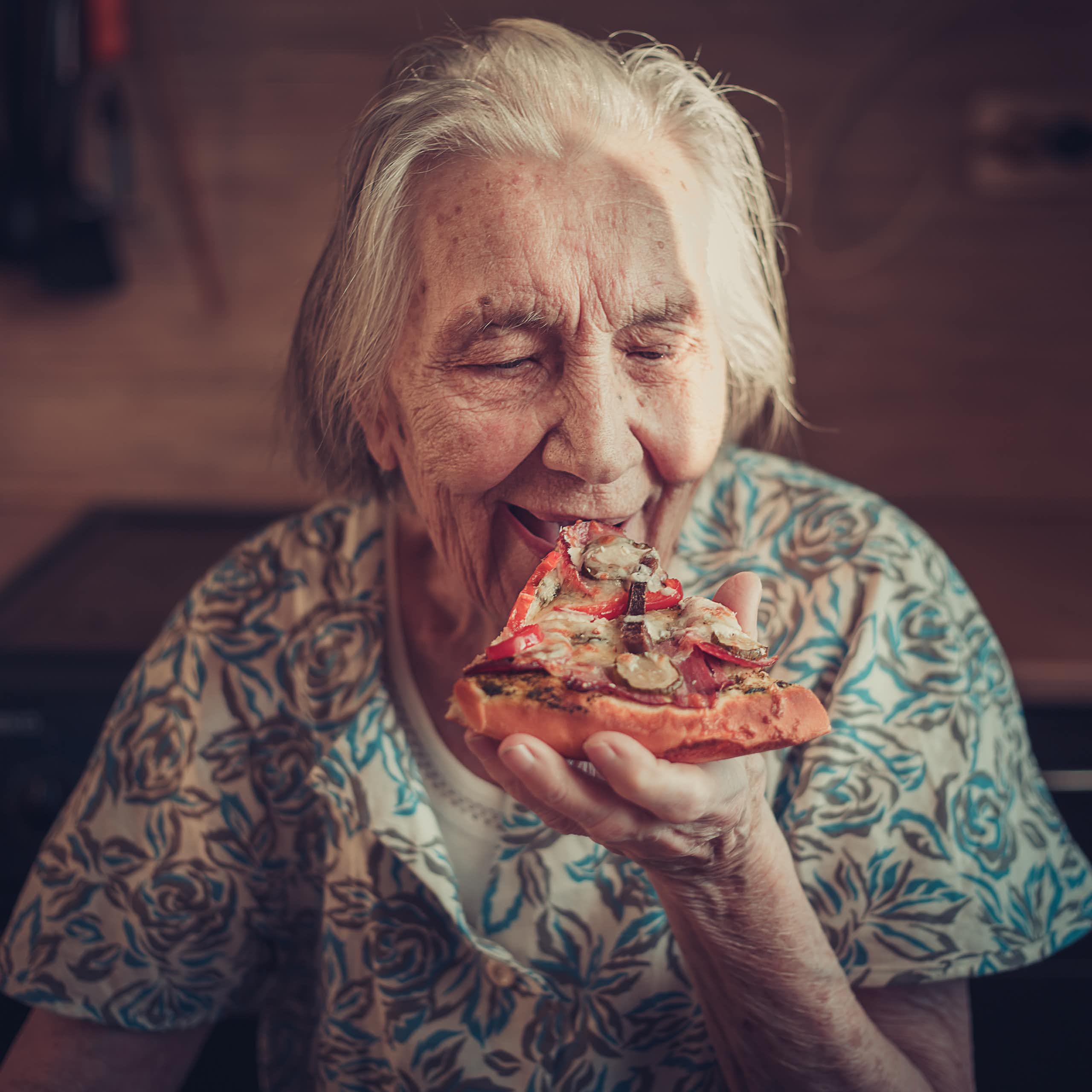 Elderly woman eating a slice of pizza