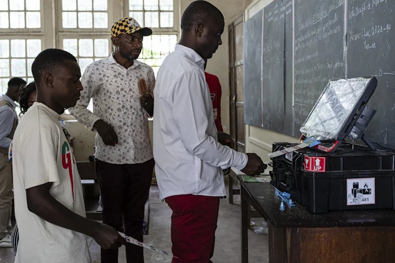 Three men stand in front of an electronic screen in a classroom