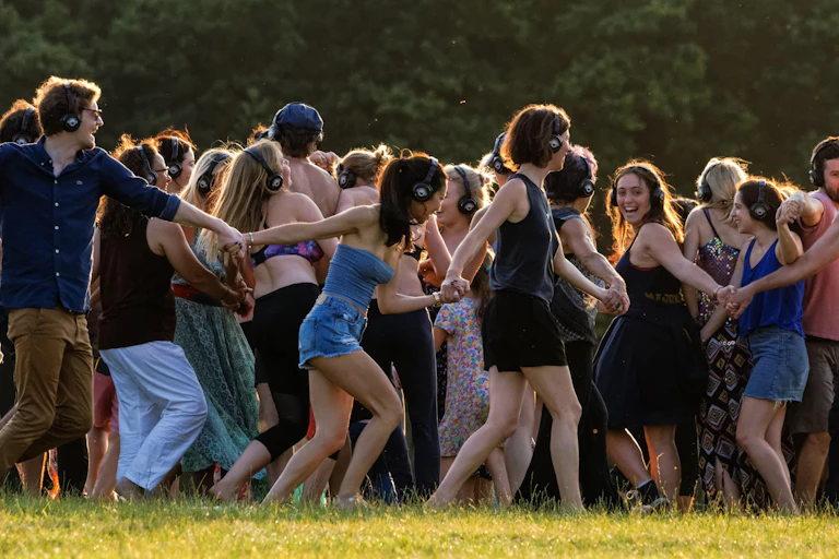 A group of young people outdoors at a festival dancing to a silent disco.