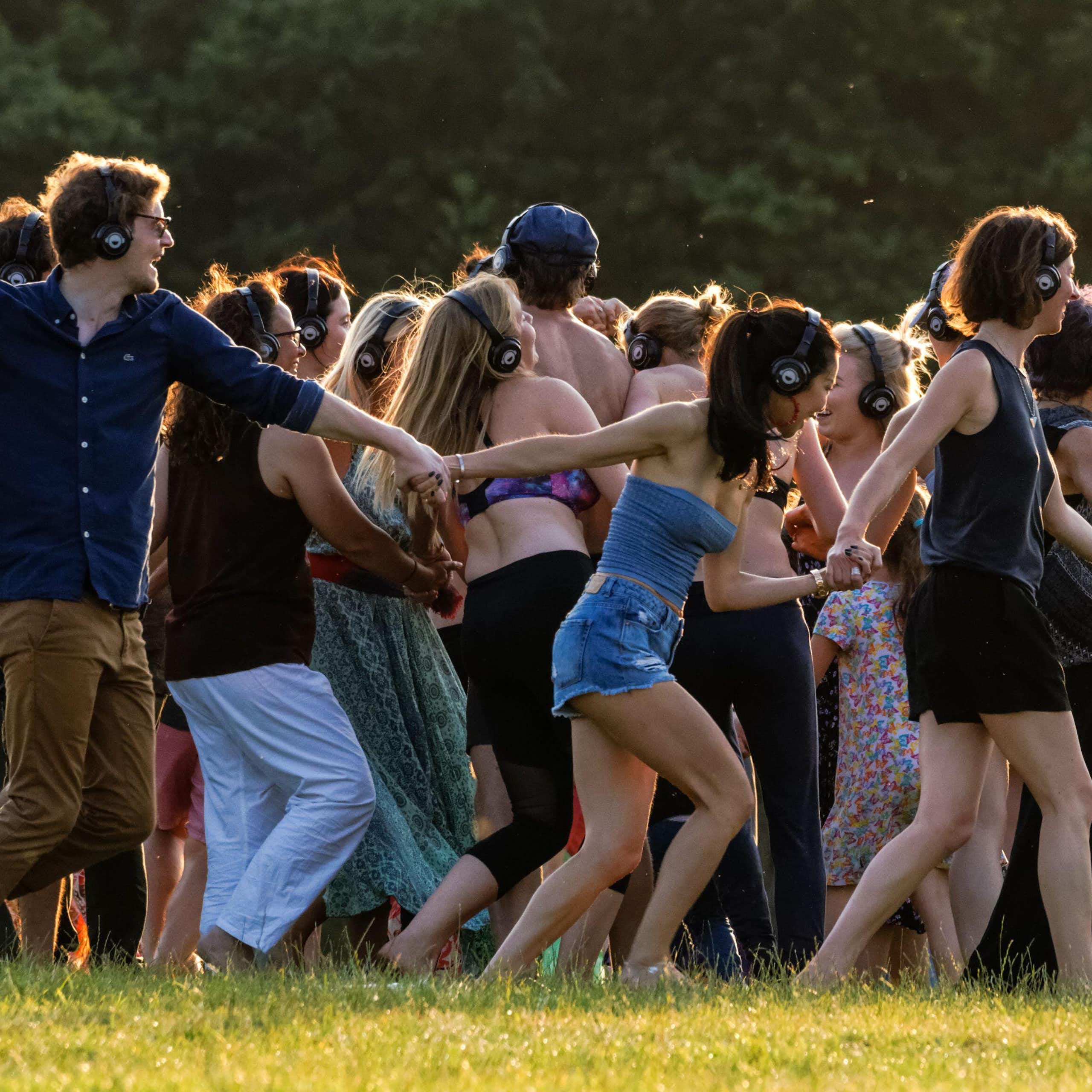 A group of young people outdoors at a festival dancing to a silent disco.