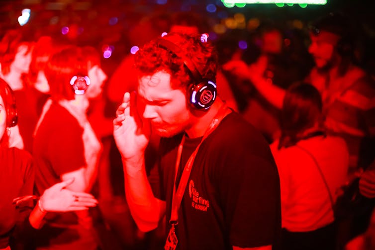 A young man dancing to a silent disco wearing headphones, illuminated by red lights.
