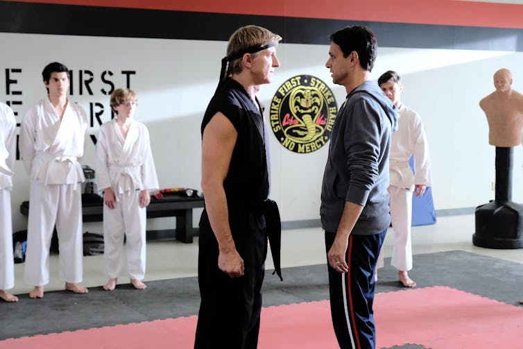 Two men stand facing each other in a karate dojo.