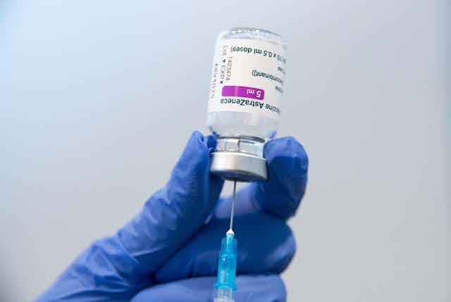 A gloved hand holding a phial of AstraZeneca vaccine