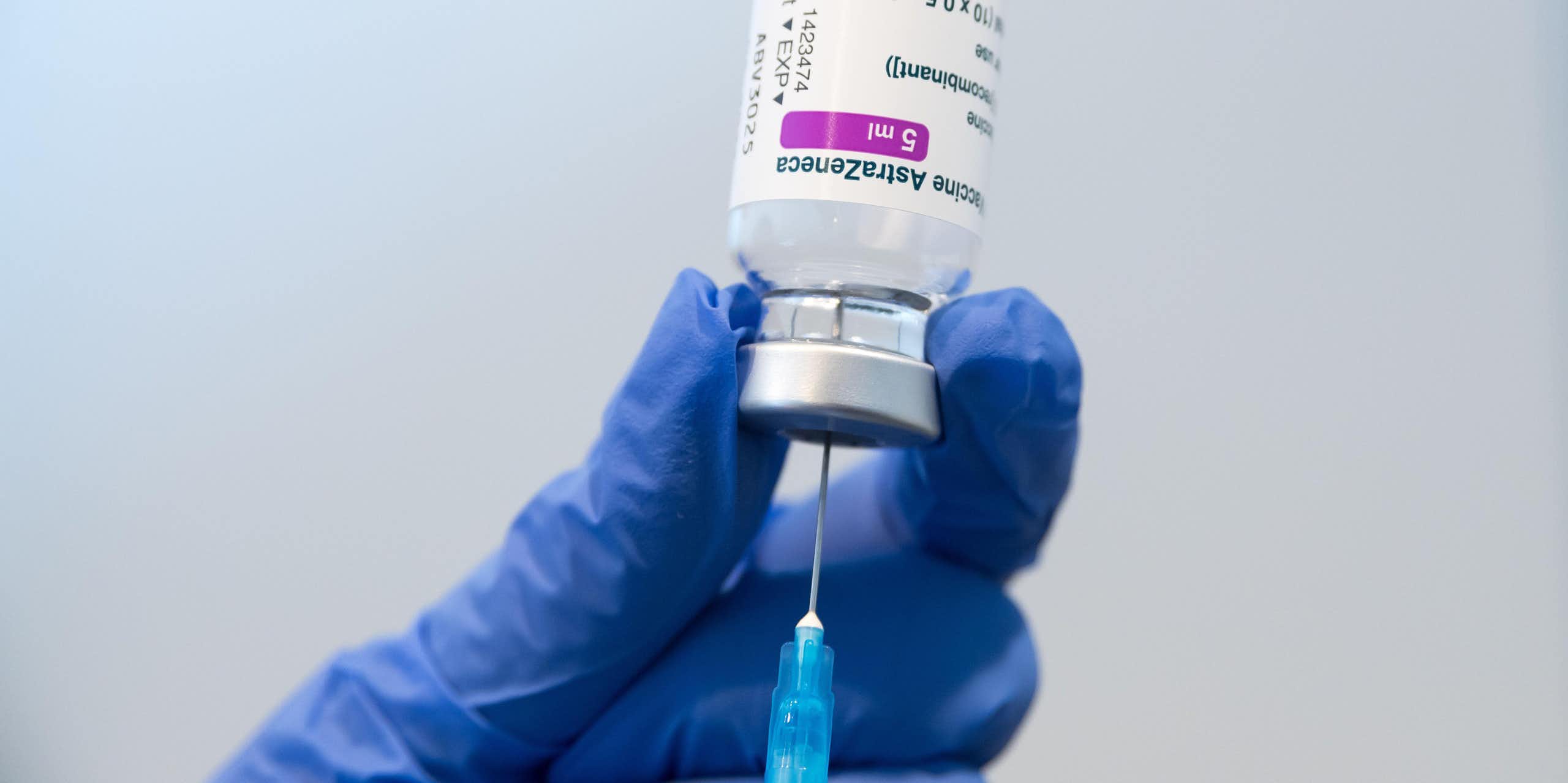 A gloved hand holding a phial of AstraZeneca vaccine