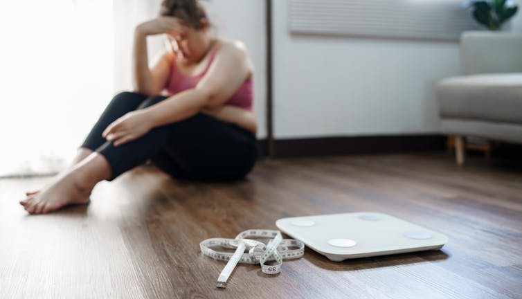 A desperate woman sits on the floor next to a scale