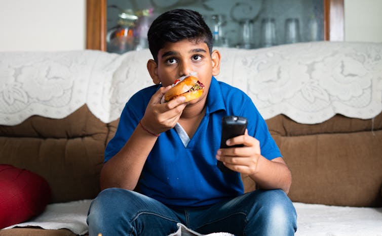 A young boy watches television while eating junk food