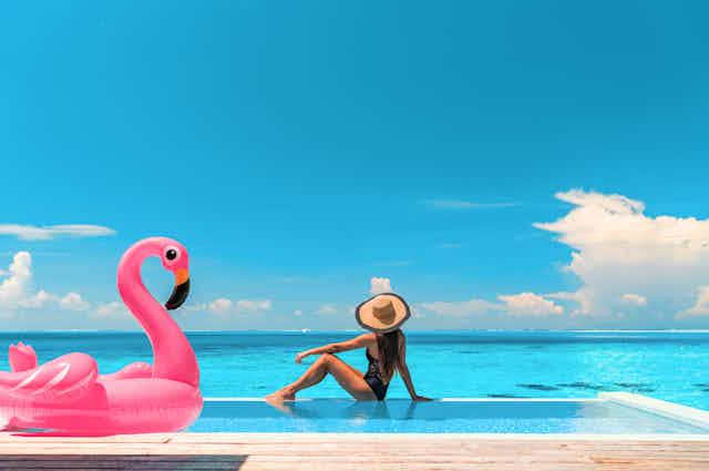 Inflatable flamingo and woman next to a swimming pool by the sea.