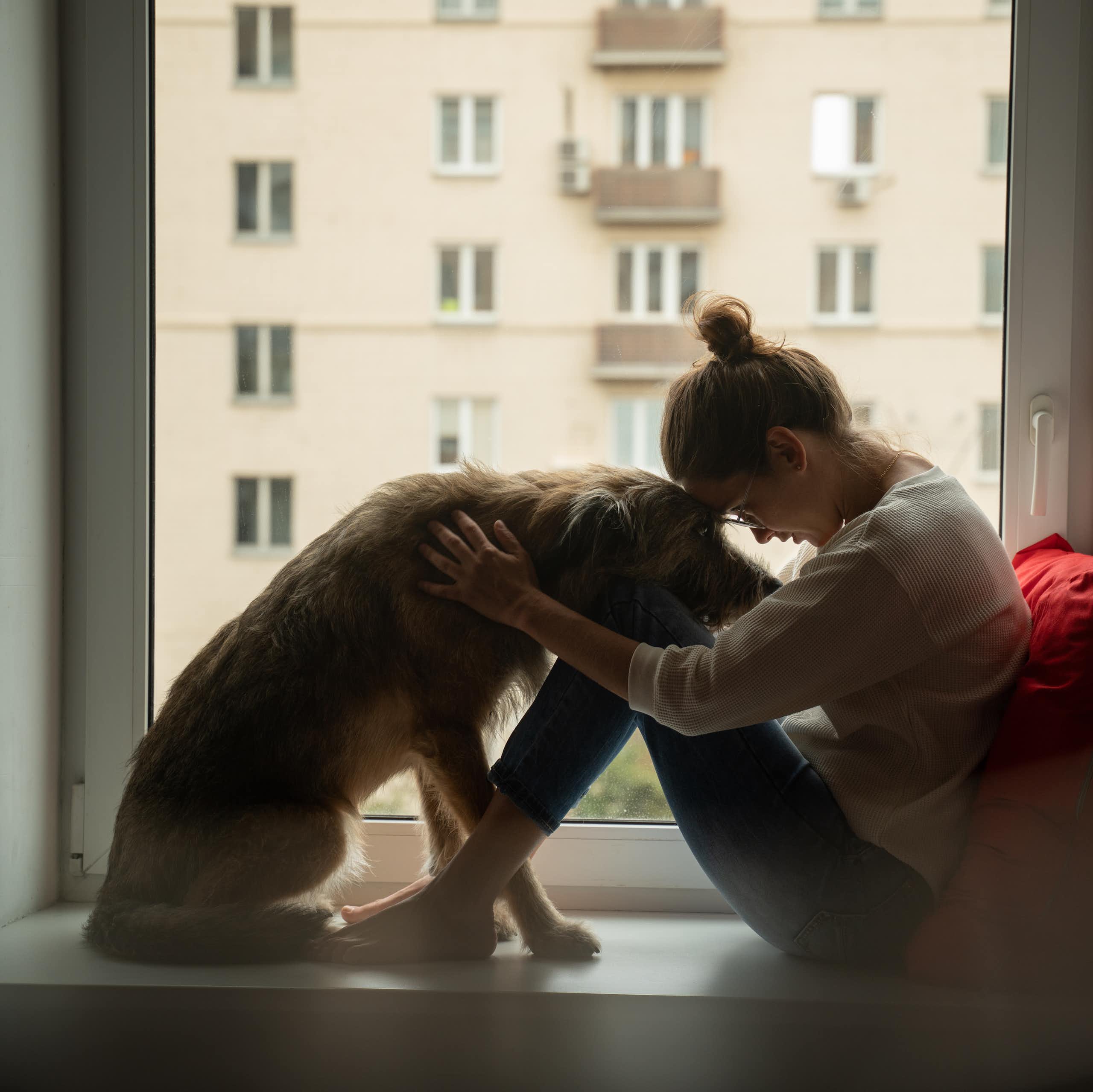 A woman and dog sitting in a dar room next to a window