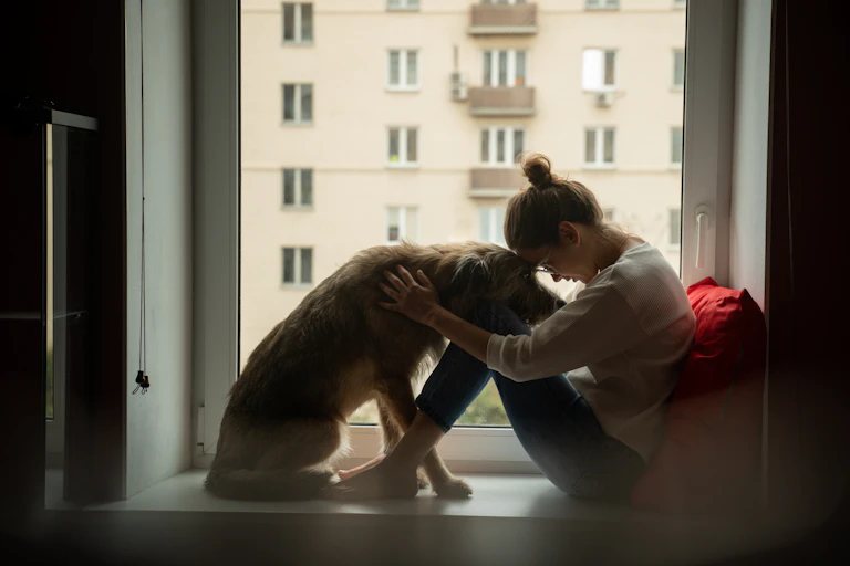 A woman and dog sitting in a dar room next to a window