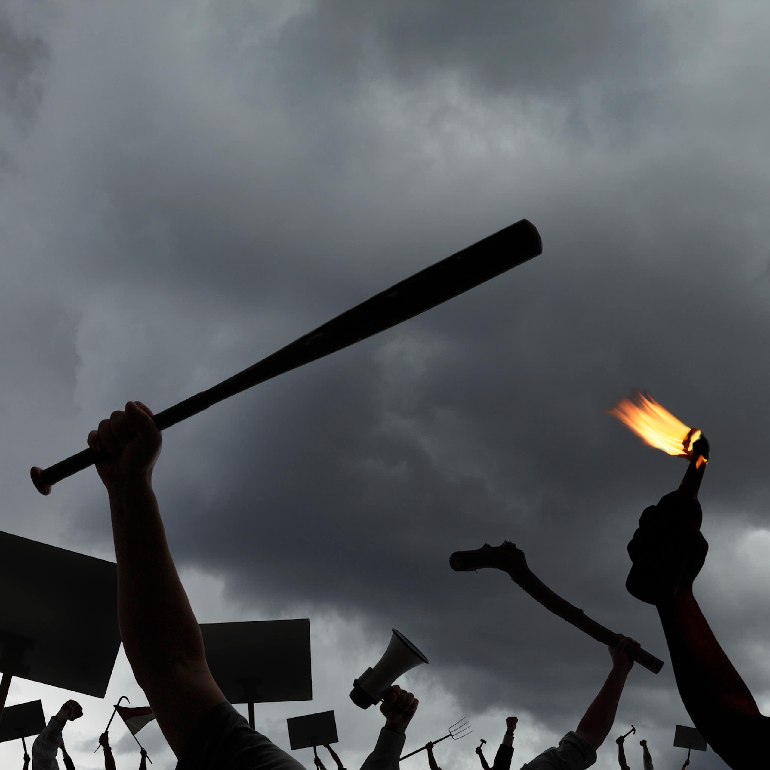 Arms of an angry mob holding protest signs, megaphones, pitchforks, molotov cocktails, and baseball bats, among other weapons